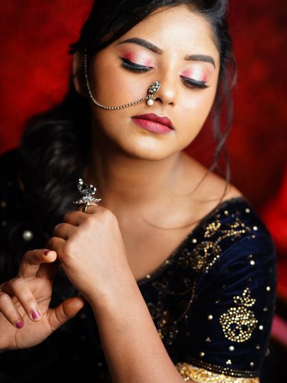 This is a powerful studio portrait designed for a model's portfolio. The focus is on the unique silver jewelry, especially the nose-to-ear chain, and the model's soft, elegant pose against a rich, dark background.