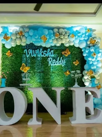 A simple and elegant first birthday setup with a grass wall, a blue and white balloon arch, and large 'ONE' letters.