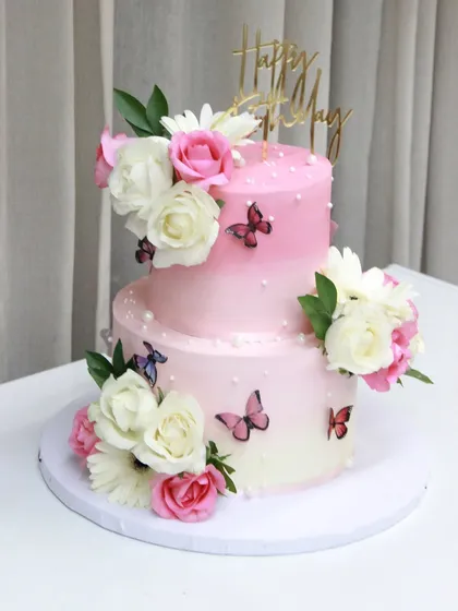 A pretty two-tiered cake for a 50th birthday, featuring ombre pink ganache, fresh flowers, and delicate wafer paper butterflies for a light and airy design.
