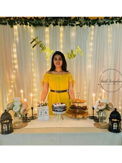 A simple yet stunning birthday setup. We created this elegant backdrop using a white curtain interwoven with warm fairy lights and a leafy garland, perfect for a classic and intimate birthday celebration at home.