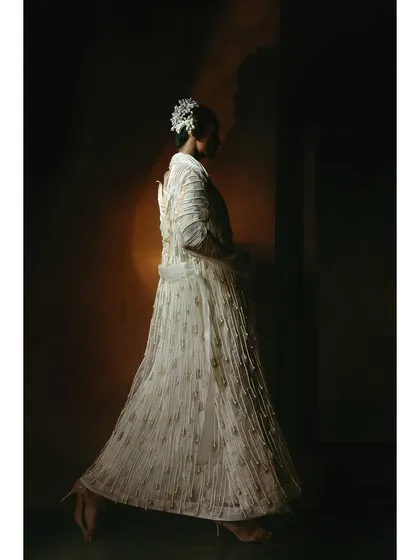 A full-length shot of a white, embroidered coat from the Vaishali S. campaign. The side profile and walking pose give the garment a sense of life and movement.