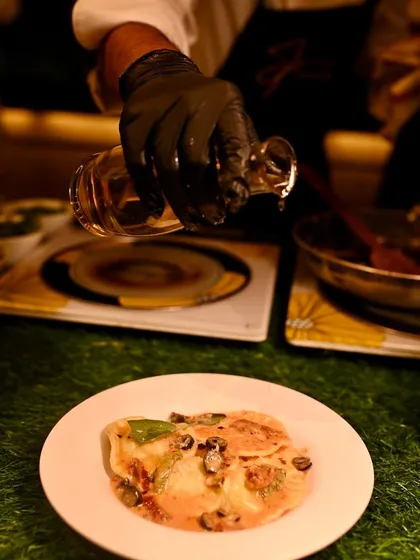 A chef adds a drizzle of olive oil to a freshly prepared plate of Spinach & Ricotta Ravioli at our live Italian station.