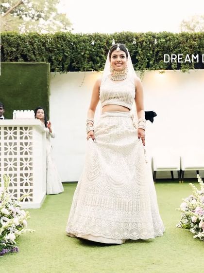 The bride's grand entrance down a green aisle lined with soft purple and white floral arrangements. The modern, clean design keeps the focus entirely on her.