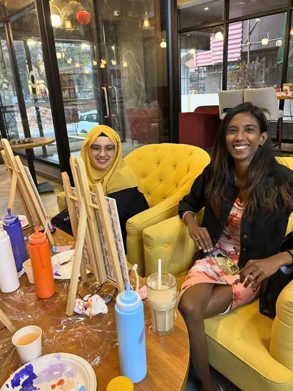 Two friends smiling and enjoying the relaxed, creative atmosphere of a sip and paint session.