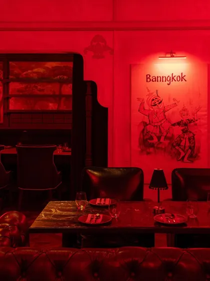 A dining table set for two, with a custom art piece depicting Thai folklore on the wall. The space is filled with narrative details that invite discovery.