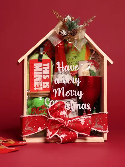 Getting cozy for the holidays with my house-shaped Christmas hamper. It’s filled with festive goodies like a 'Be Merry & Bright' glass, a non-alcoholic beverage, and other treats, all wrapped up with a festive red ribbon.