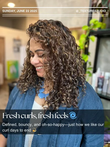 Fresh curls, fresh feels. This happy client is glowing after her curly cut and styling session, showing off defined, bouncy curls with beautiful highlights.