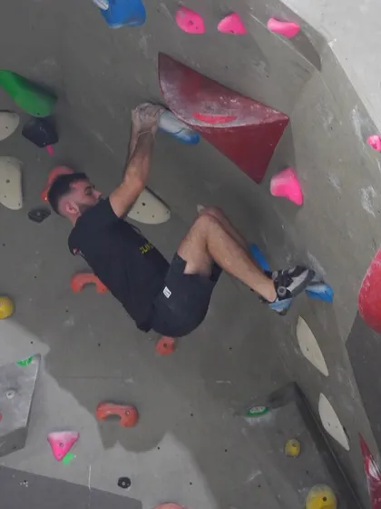 A climber hangs on, fully engaged, while navigating a difficult section with red volumes. This demonstrates the strength needed for overhanging bouldering problems.