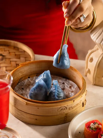 A beautiful blue pea flower dumpling being picked up with chopsticks. The unique color makes it a perfect hero shot for a special menu item.