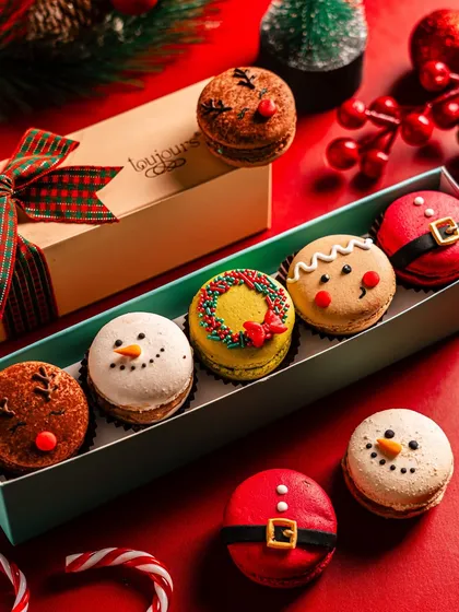 A box of six adorable Christmas macarons, featuring designs like a snowman, gingerbread man, and Santa's suit. This is a perfect small gift or stocking stuffer for the macaron lover in your life.