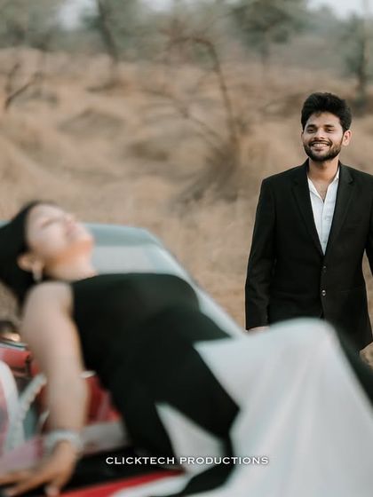 A candid and happy moment during a vintage car photoshoot, with the groom smiling as the bride relaxes on the car's hood.