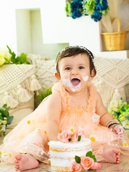A picture of pure delight. Her face says it all as she enjoys her beautiful floral cake in a lovely boho-themed setup for her first birthday.