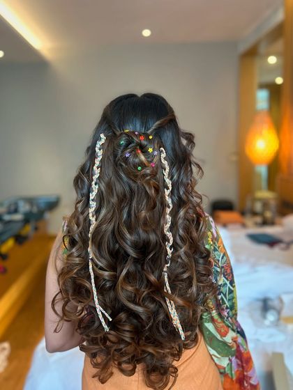 A playful and boho half-up, half-down style with bouncy curls and fun, colorful accessories, perfect for a Mehendi party.