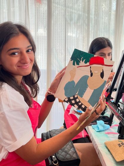 A young girl smiling with her finished painting at a cafe workshop. I make sure my workshops are welcoming and fun for all ages.