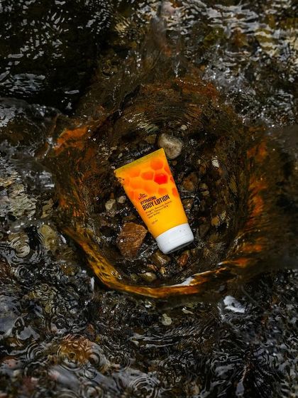 A skincare product shot in its natural element. This body lotion tube is placed in the middle of a flowing stream, creating a dynamic and refreshing image that speaks to natural hydration.