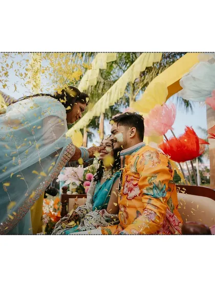 A beautiful moment where a family member applies haldi to the couple, with a shower of flower petals creating a magical effect.