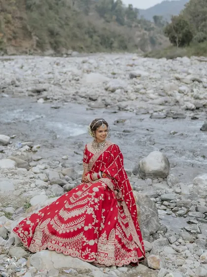 A serene portrait of the bride sitting on a rock by the river, her red lehenga a vibrant splash of color.