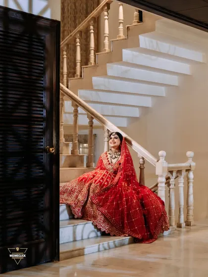 A beautiful portrait of the bride sitting on a grand marble staircase, her red lehenga spread out, creating a look of regal elegance.