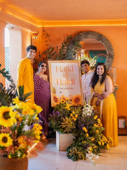 The family poses by the "Halki si Haldi" sign. I styled them in a color palette of yellows and purples, which coordinated beautifully with the sunflower decor. It shows how outfits can tie into the overall event theme.