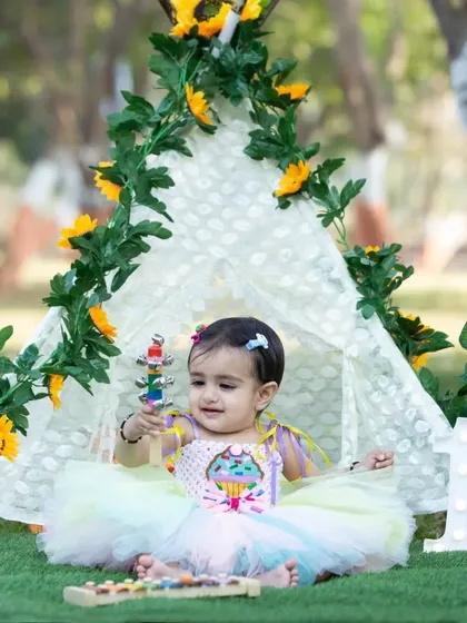 A happy baby girl playing in front of a teepee decorated with sunflowers.