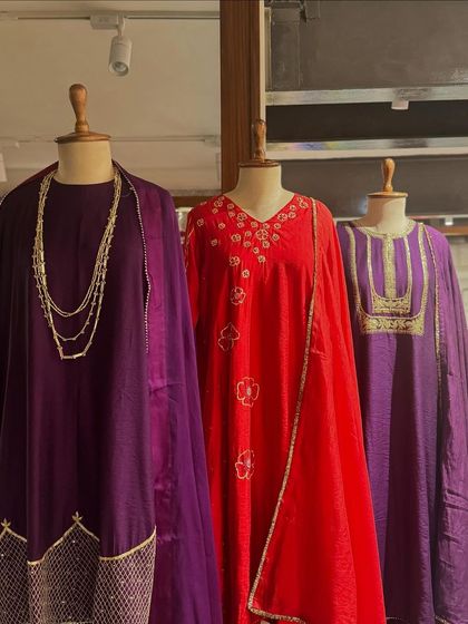 A trio of festive suits in jewel tones of purple and red, featuring gold embroidery and flowing dupattas.