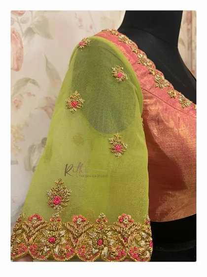 A detailed view of a sheer green sleeve with pink and gold floral embroidery. The cutwork border on the cuff adds another layer of intricacy.