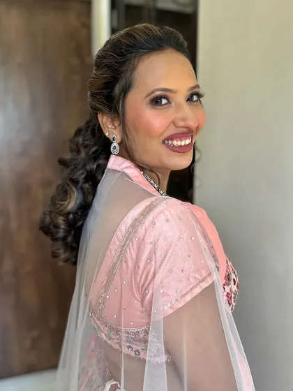 A happy, over-the-shoulder smile. The client looks ready for her event, with a curly ponytail and soft pink makeup.