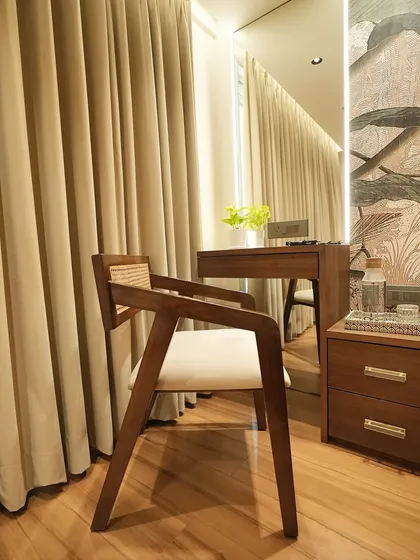 Another angle of the elegant wooden and rattan chair, placed next to a vanity. Its timeless design complements the warm wooden floors and soft curtains, adding to the room's serene atmosphere.