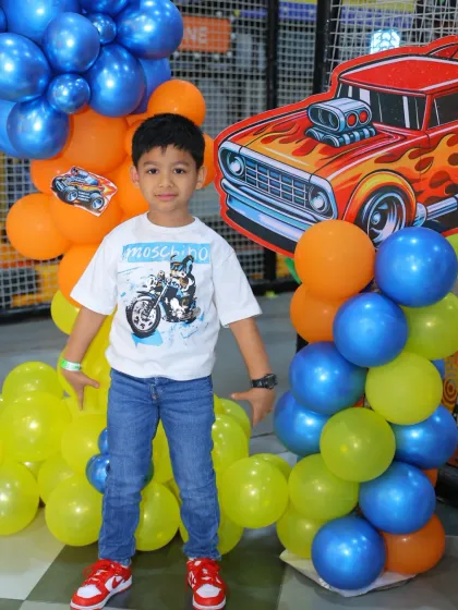 The birthday boy and his mom pose by the colorful balloon arch at his Hot Wheels party.