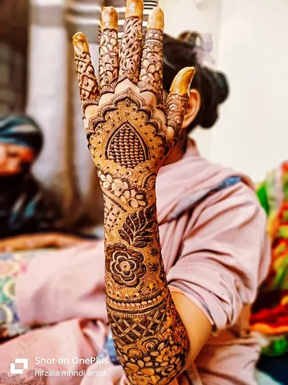 Bride Sunera showing off her full bridal arm design. The pattern includes a mix of florals, leaves, and traditional Indian grid work.