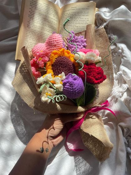 The "Lover's Bouquet" held in hand, styled with an open book for a romantic, literary feel. The mix of colors and flowers makes it a truly special arrangement.