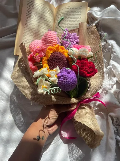 The "Lover's Bouquet" held in hand, styled with an open book for a romantic, literary feel. The mix of colors and flowers makes it a truly special arrangement.