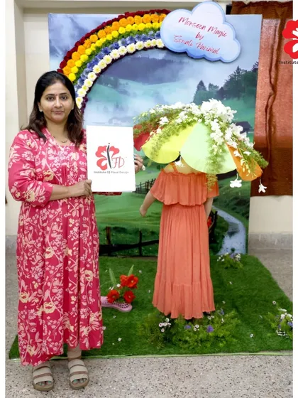 This graduate's final project, "Monsoon Magic," is a joyful and creative installation. It features a mannequin with a floral umbrella under a rainbow of flowers, capturing a complete and imaginative theme.