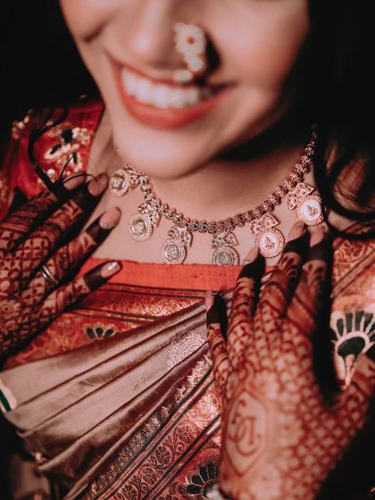 A creative shot focusing on the bride's smile and her traditional coin necklace (putli haar). The intricate mehendi on her hands frames the shot beautifully.