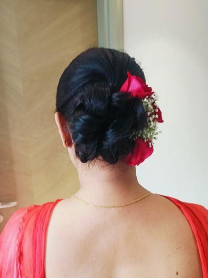 A side view of a classic floral bun, showing how the red rose and baby's breath are carefully integrated. This angle highlights the neatness and structure of the bridal updo.