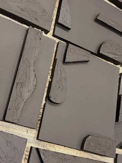A detailed shot of the black acrylic-on-board panels. You can see the contrast between the smooth, matte finish of the board and the rough, tactile quality of the raised sculptural elements.