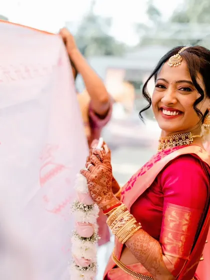 A candid moment from a beautiful South Indian wedding. The bride's smile says it all. Her makeup is kept fresh and luminous to complement the vibrant pink Kanjeevaram saree, paired with a classic bridal updo.