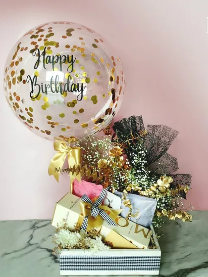 A classic birthday hamper that brings the celebration. It includes a festive 'Happy Birthday' balloon, a stylish checkered box filled with luxury essentials like Moët & Chandon, and a chic black and gold floral arrangement.