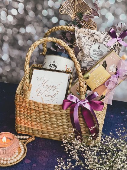My 'Tyohaar' hamper celebrates Diwali sustainably with a handmade cane basket from local artisans. It's filled with handpicked gourmet snacks and a 'Happy Diwali' card, all in a beautiful lilac and purple color scheme.