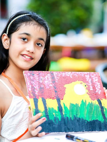 A proud young artist displaying her beautiful sunset painting, created during the canvas painting session at the art party.