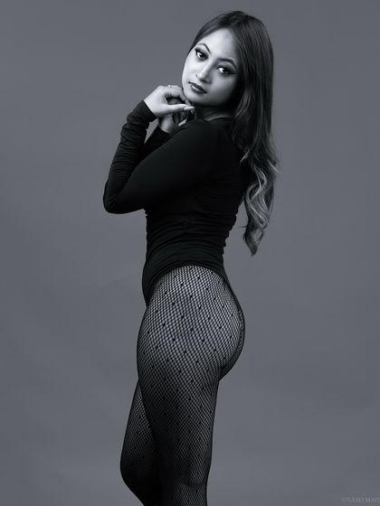 A three-quarter monochrome portrait in a classic bodysuit and patterned stockings. The lighting is soft, creating a gentle and elegant mood.