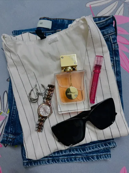 This flat lay shows the components of an easy-to-wear daily outfit. A striped waistcoat, comfortable jeans, and essential accessories like a watch, sunglasses, and perfume are all you need for a stylish day.