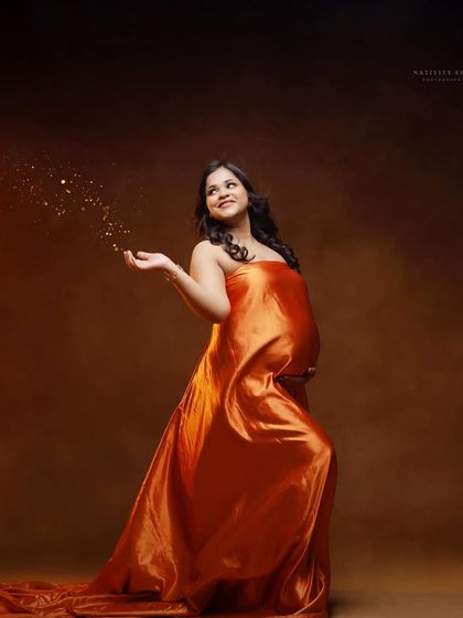 A joyful solo portrait of the mother-to-be tossing glitter. The warm tones of the orange gown and the studio backdrop create a celebratory feel.