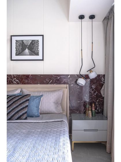 The master bedroom in the Plush Abode project is adorned with a statement Rosso Levanto stone wall. The bed, finished in natural veneer, creates a luxurious and dramatic focal point in this contemporary residential design.