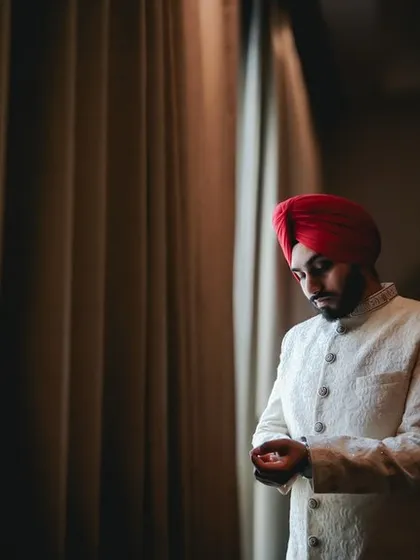 A classic groom portrait. The groom, wearing a traditional turban, adjusts his sleeve in a moment of quiet preparation.