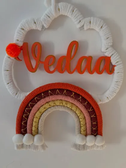 A simple, clean shot of the 'Vedaa' name hanging, focusing on the personalized name and the cute pom-pom details.