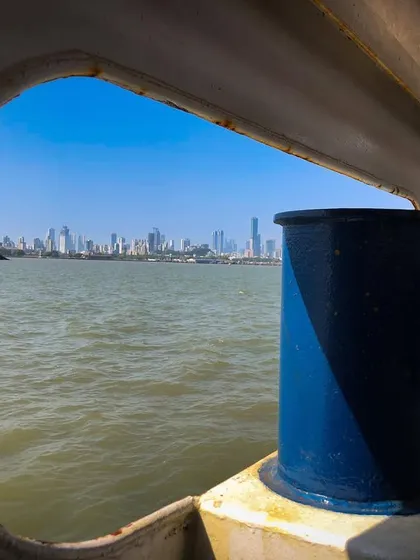 The Mumbai skyline is framed perfectly through the window of a ferry, creating a sense of being "so close yet so far."