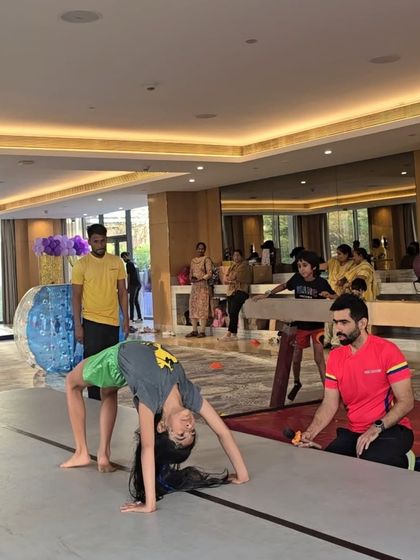 A girl practices a backbend on the air mat with a coach spotting her. The soft landing surface gives kids the confidence to try new and challenging moves.