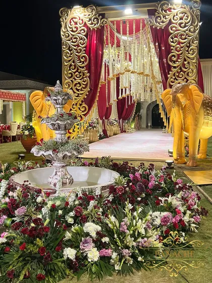 A stunning fountain surrounded by a bed of maroon and white flowers serves as a central focal point. It adds a dynamic and refreshing element to the opulent outdoor setting.