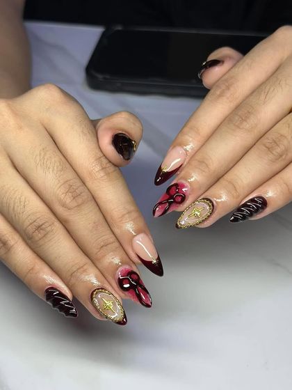 A dark and glamorous design. These stiletto nails feature a deep red and black base with intricate 3D elements and gold star accents.